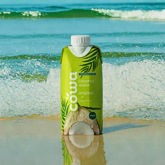 Cowa Coconut juice bottle on beach sand with ocean background – beverage photography.