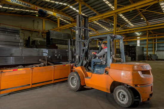 Worker unloading steel pipes from truck in factory