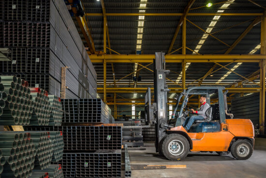 Forklift moving steel pipes inside warehouse