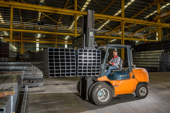 Forklift moving steel pipes inside warehouse