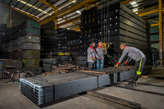Workers stacking metal pipes inside factory