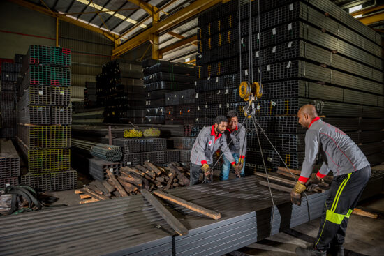 Factory workers loading steel pipes in warehouse